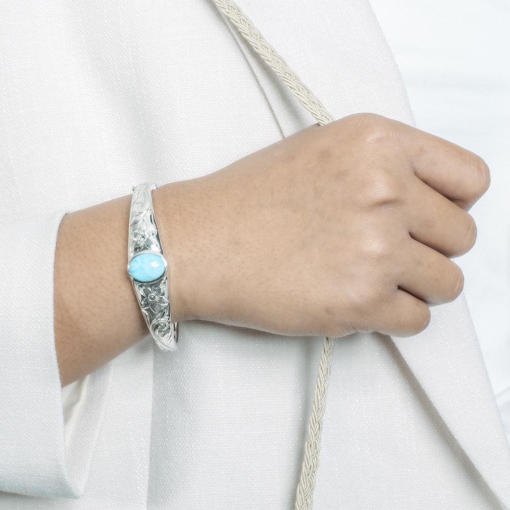 In this photo there is a model wearing a 925 sterling silver bangle with one blue larimar gemstone and plumeria engravings.