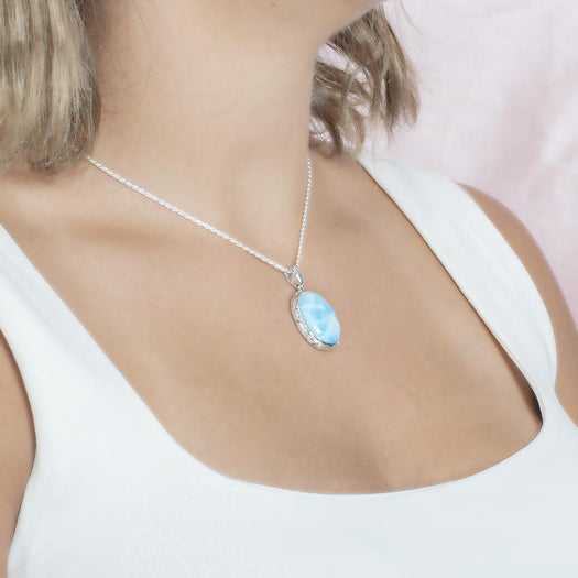 The picture shows a model wearing a 925 sterling silver oval larimar pendant with hand engravings.