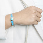 The picture shows a model wearing a 925 sterling silver bangle with one larimar gemstone centered by two opalite gemstones.