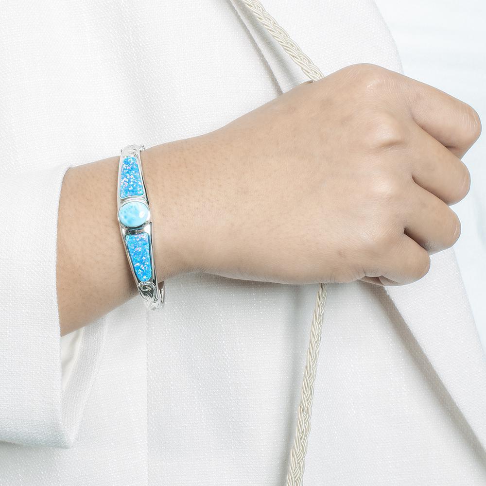 The picture shows a model wearing a 925 sterling silver bangle with one larimar gemstone centered by two opalite gemstones.