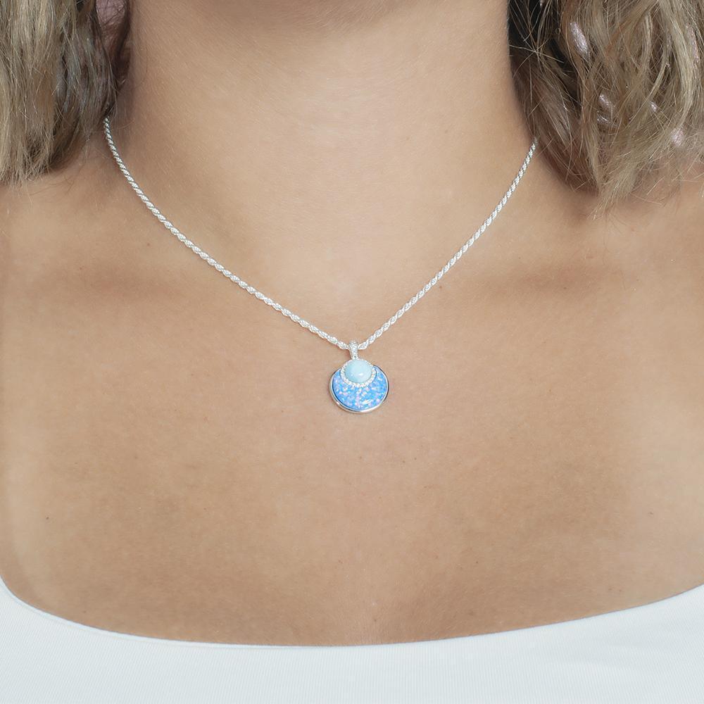 In this photo there is a model with blonde hair and a white shirt, wearing a sterling silver circle pendant with blue larimar, opalite, and topaz gemstones.