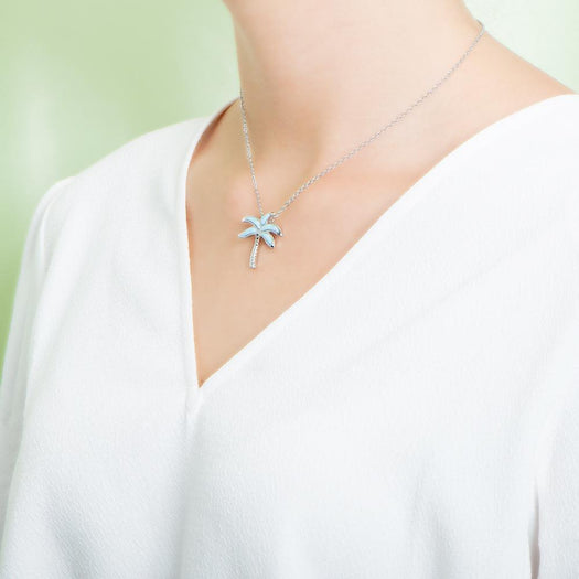 In this picture there is a model faced to the left with a white shirt, wearing a palm tree pendant with blue larimar gemstones set in sterling silver.