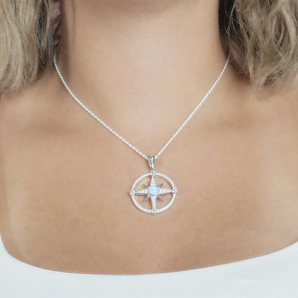In this photo there is model with blonde hair and a white shirt, wearing a sterling silver compass pendant with blue larimar and topaz gemstones.