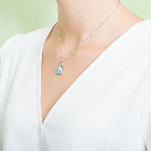 In this photo there is a model turned to the left with a white shirt, wearing a sterling silver pineapple pendant with one blue larimar gemstone.