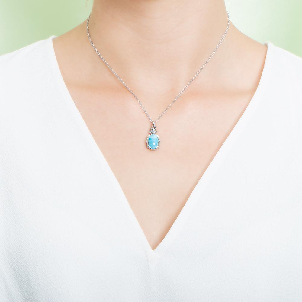 In this photo there is a model with a white shirt wearing a sterling silver pineapple pendant with one blue larimar gemstone.