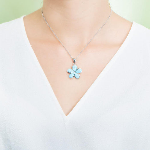 In this photo there is a model with a white shirt wearing a medium sized sterling silver plumeria pendant with blue larimar gemstones.
