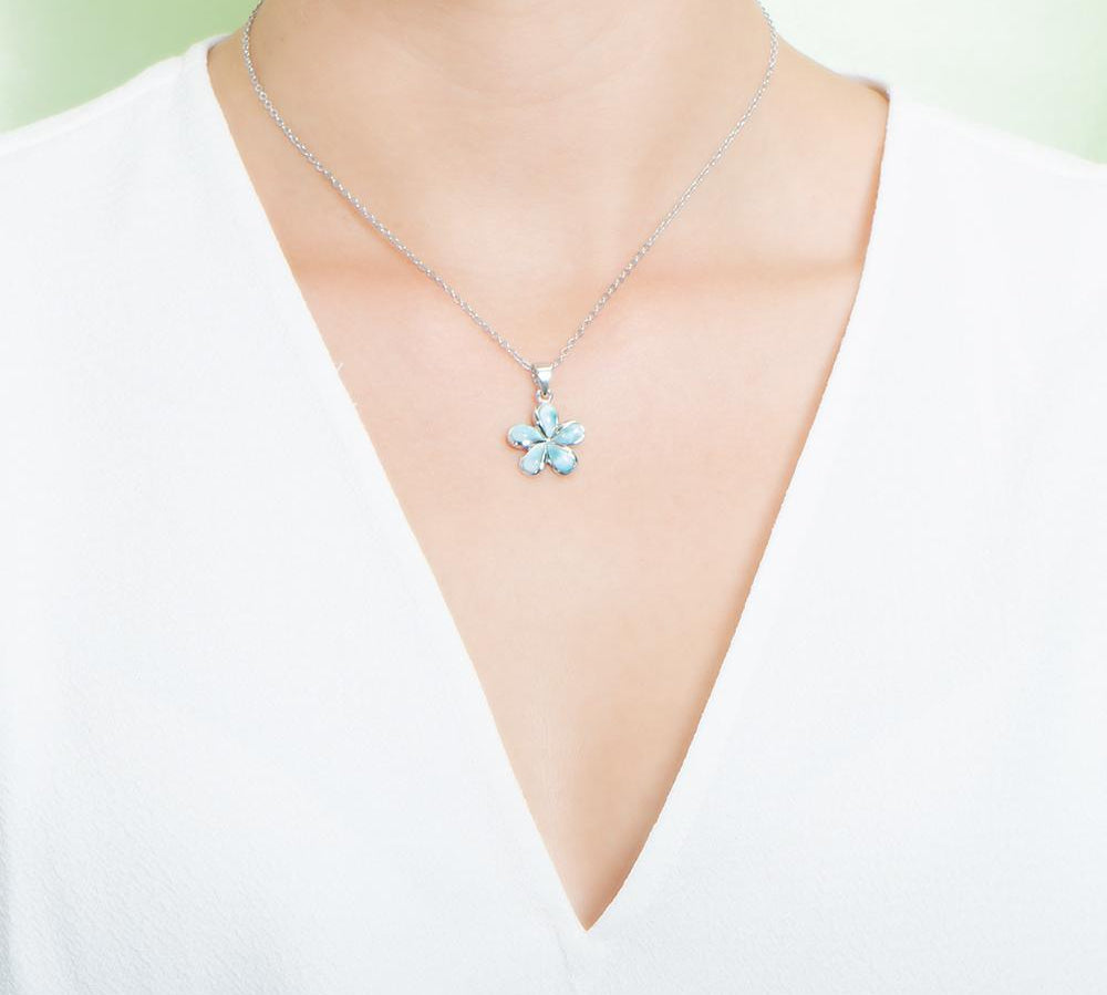 In this photo there is a model with a white shirt wearing a small sterling silver plumeria pendant with blue larimar gemstones.