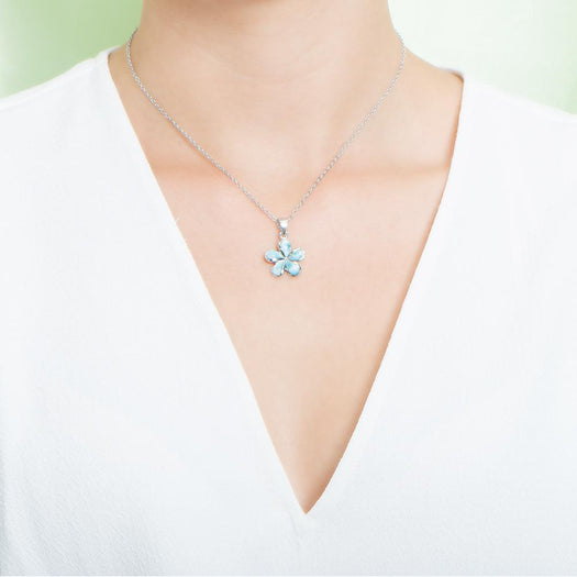 In this photo there is a model with a white shirt wearing a small sterling silver plumeria pendant with blue larimar gemstones.