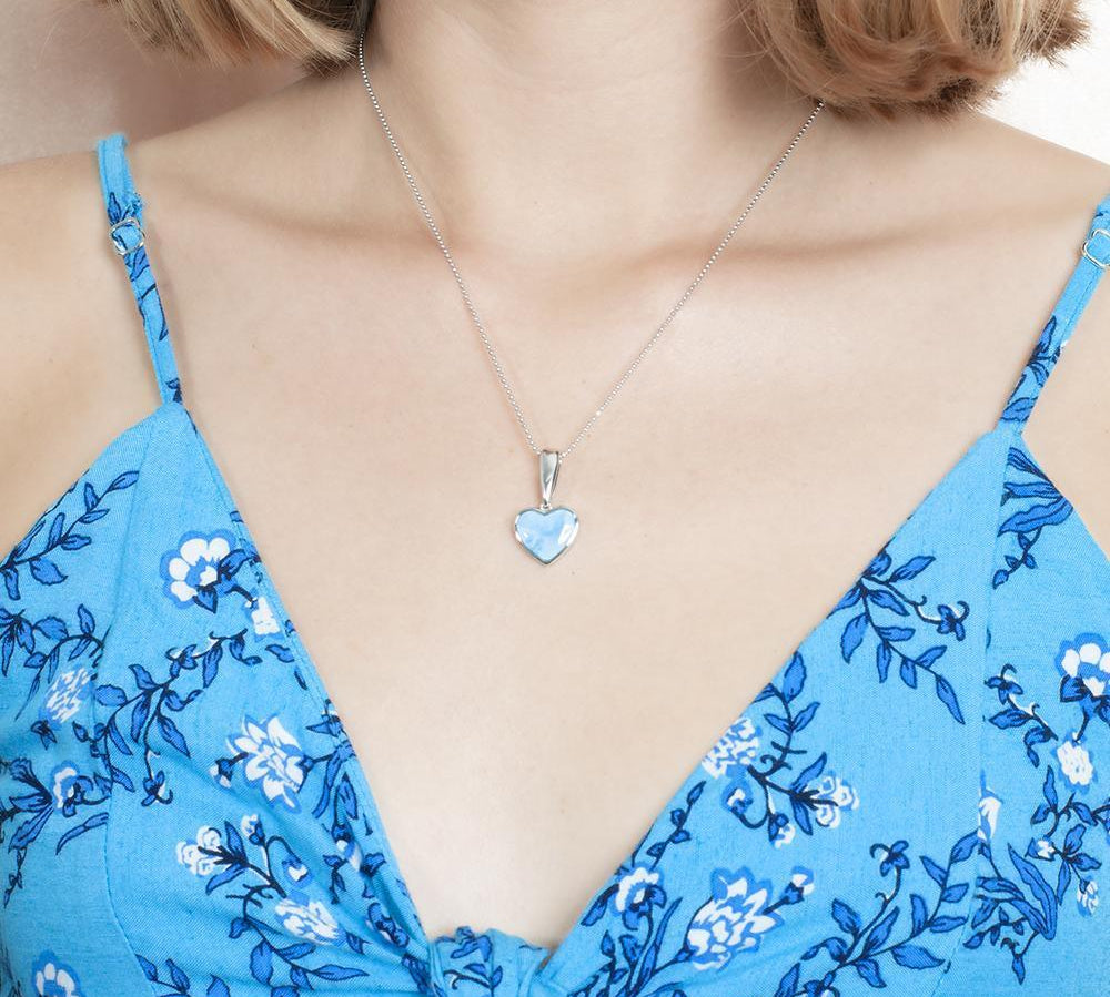 The picture shows a model wearing a 925 sterling silver larimar heart pendant and a blue dress.