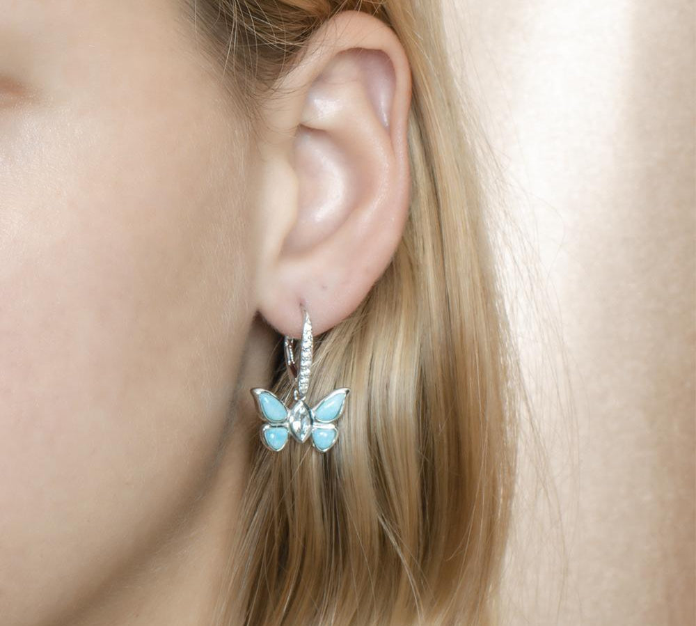 In this photo is a model wearing a 925 sterling silver butterfly lever-back earring with blue larimar, topaz, and aquamarine gemstones.