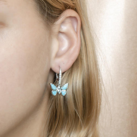 In this photo is a model wearing a 925 sterling silver butterfly lever-back earring with blue larimar, topaz, and aquamarine gemstones.