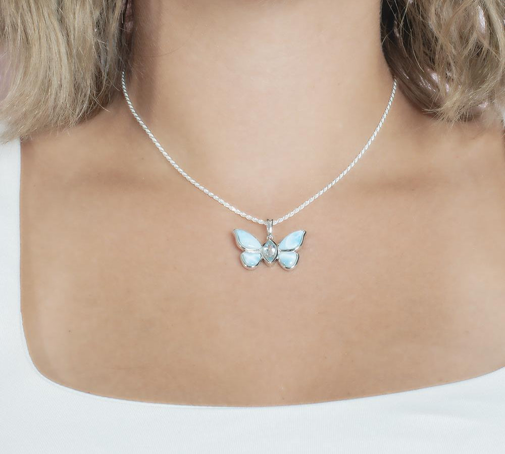 In this photo there is a model with blonde hair and a white shirt, wearing a sterling silver butterfly pendant with blue larimar gemstones and aquamarine.