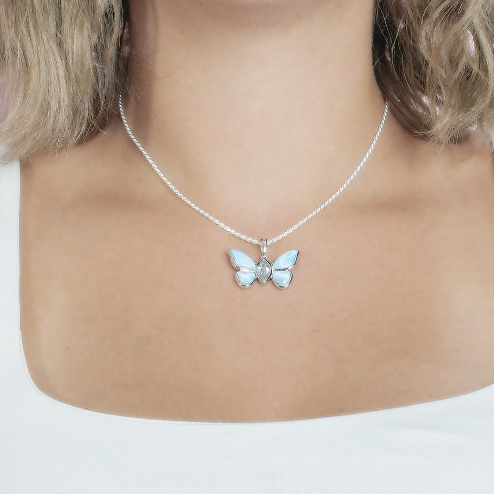 In this photo there is a model with blonde hair and a white shirt, wearing a sterling silver butterfly pendant with blue larimar gemstones and aquamarine.