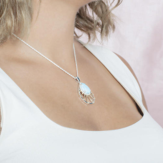 In this photo there is a model with blonde hair and a white shirt turned to the right, wearing a sterling silver and gold plated tear drop pendant with topaz, aquamarine, and one blue larimar gemstone.