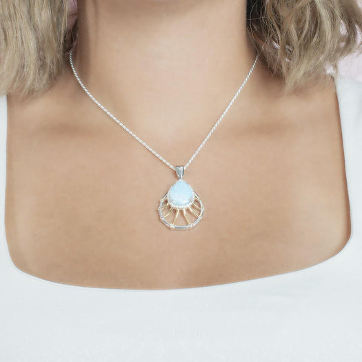 In this photo there is a model with blonde hair and a white shirt wearing a sterling silver and gold plated tear drop pendant with topaz, aquamarine, and one blue larimar gemstone.