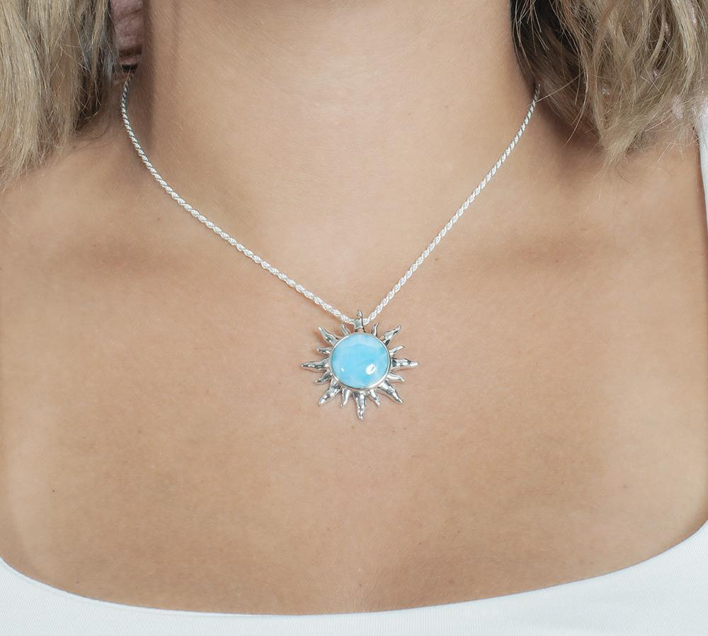 In this picture there is a model with blonde hair and a white shirt wearing a sun pendant with a blue larimar gemstone set in sterling silver.