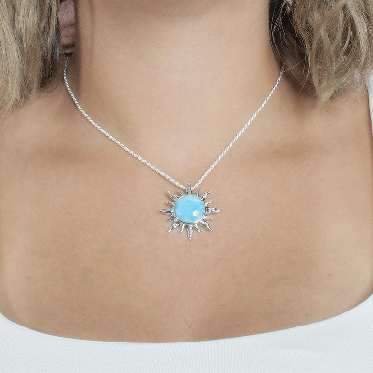 In this picture there is a model with blonde hair and a white shirt wearing a sun pendant with a blue larimar gemstone set in sterling silver.