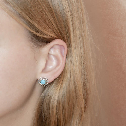 In this photo is a model wearing a 925 sterling silver sunflower stud earring with a blue larimar gemstones.