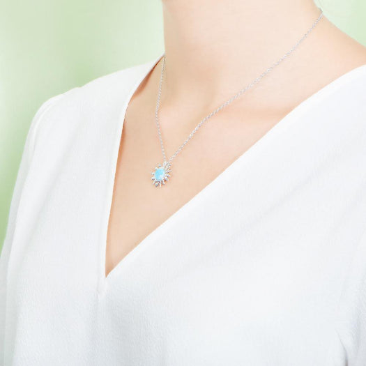 In this photo there is a model turned to the left with a white shirt, wearing a sterling silver sunflower pendant with one blue larimar gemstone.