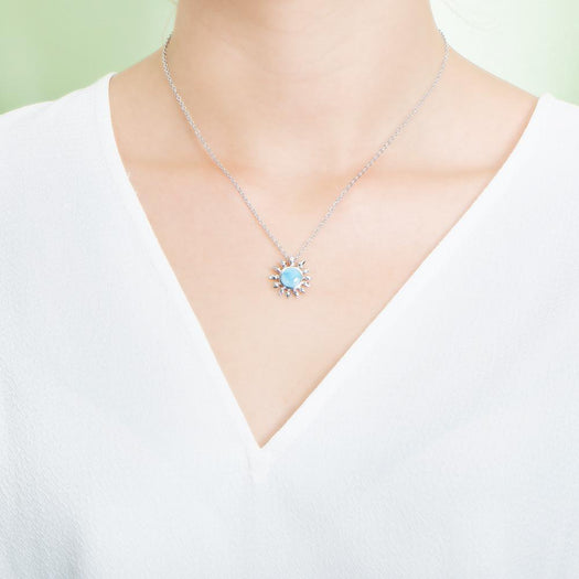 In this photo there is a model with a white shirt wearing a sterling silver sunflower pendant with one blue larimar gemstone.