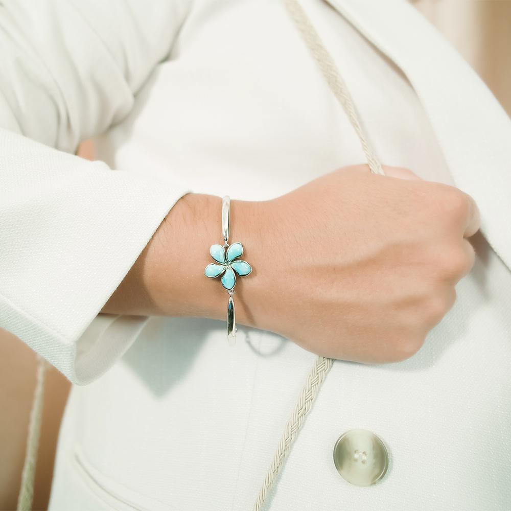 In this photo there is a model wearing a 925 sterling silver plumeria bracelet with blue larimar gemstones.