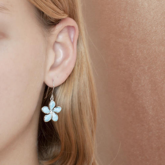 In this photo there is a model wearing a 925 sterling silver plumeria hook earring with blue larimar gemstones.