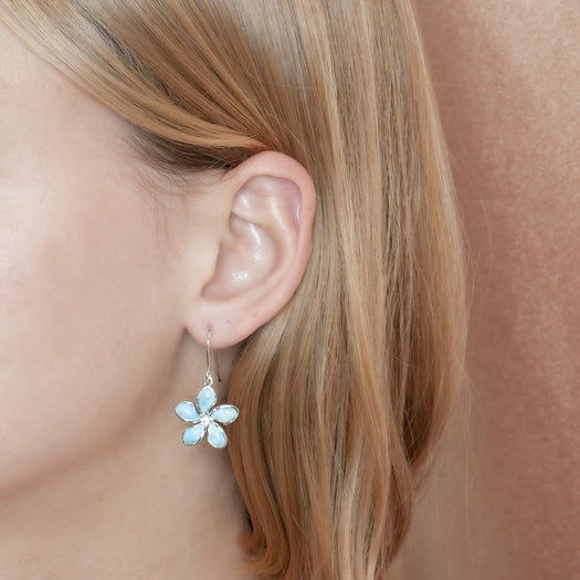 In this photo there is a model wearing a 925 sterling silver plumeria hook earring with blue larimar gemstones.