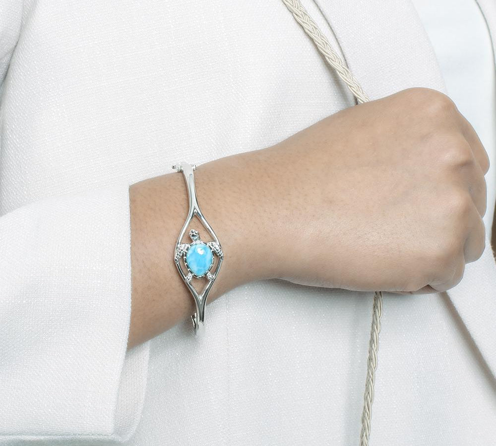 The picture shows a model wearing a 925 sterling silver larimar swimming sea turtle bangle with topaz.
