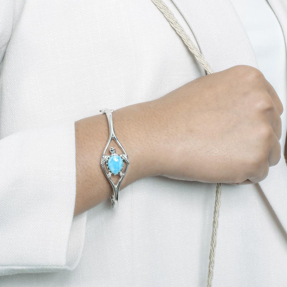 The picture shows a model wearing a 925 sterling silver larimar swimming sea turtle bangle with topaz.