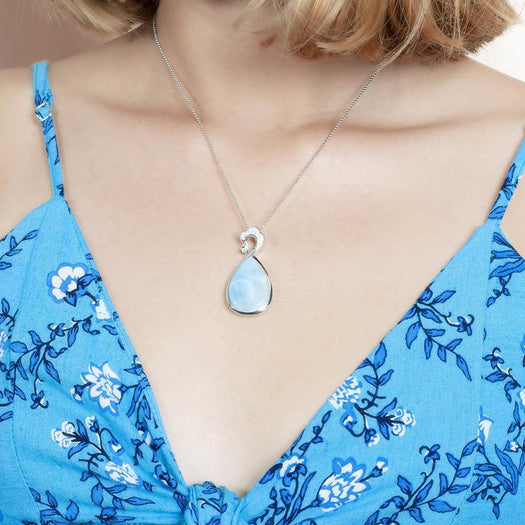 The picture shows a model wearing a 925 sterling silver larimar teardrop wave pendant with aquamarine and topaz.