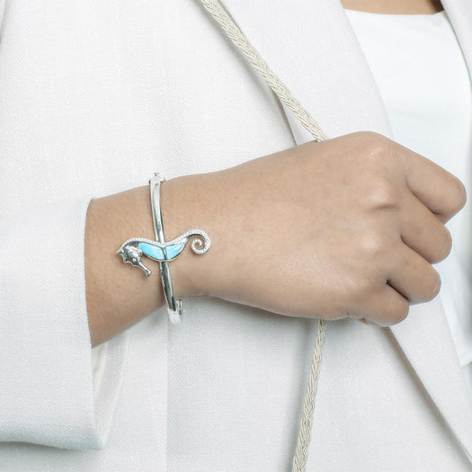 The picture shows a model wearing a 925 sterling silver larimar seahorse bangle with topaz.