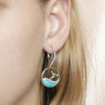 The picture shows a model wearing a 925 sterling silver larimar whale wave lever-back earring with topaz.