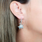 The picture shows a model wearing a 925 sterling silver sea turtle lever-back earring with topaz.