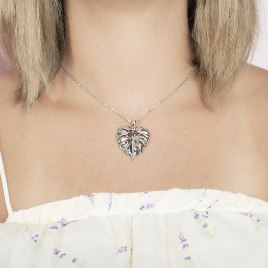 In this photo there is a model with blonde hair and white shirt with flowers, wearing a sterling silver monstera pendant.