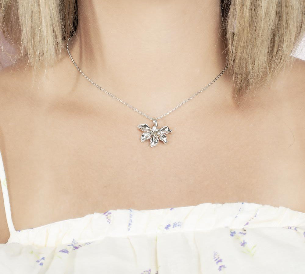 In this photo there is a model with blonde hair and a white shirt with purple flowers, wearing a sterling silver naupaka flower pendant with cubic zirconia.