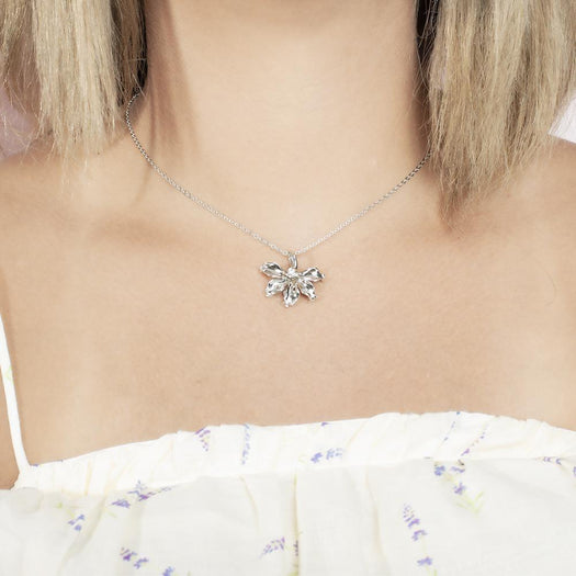 In this photo there is a model with blonde hair and a white shirt with purple flowers, wearing a sterling silver naupaka flower pendant with cubic zirconia.