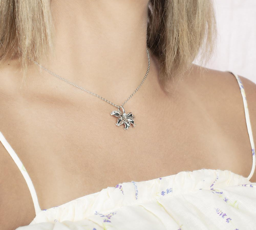 In this photo there is a model turned to the right with blonde hair and a white shirt with purple flowers, wearing a sterling silver naupaka flower pendant with cubic zirconia.