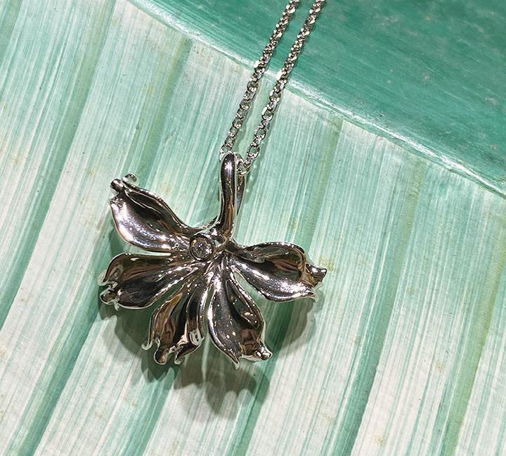 In this photo there is a white gold naupaka flower pendant with one diamond.