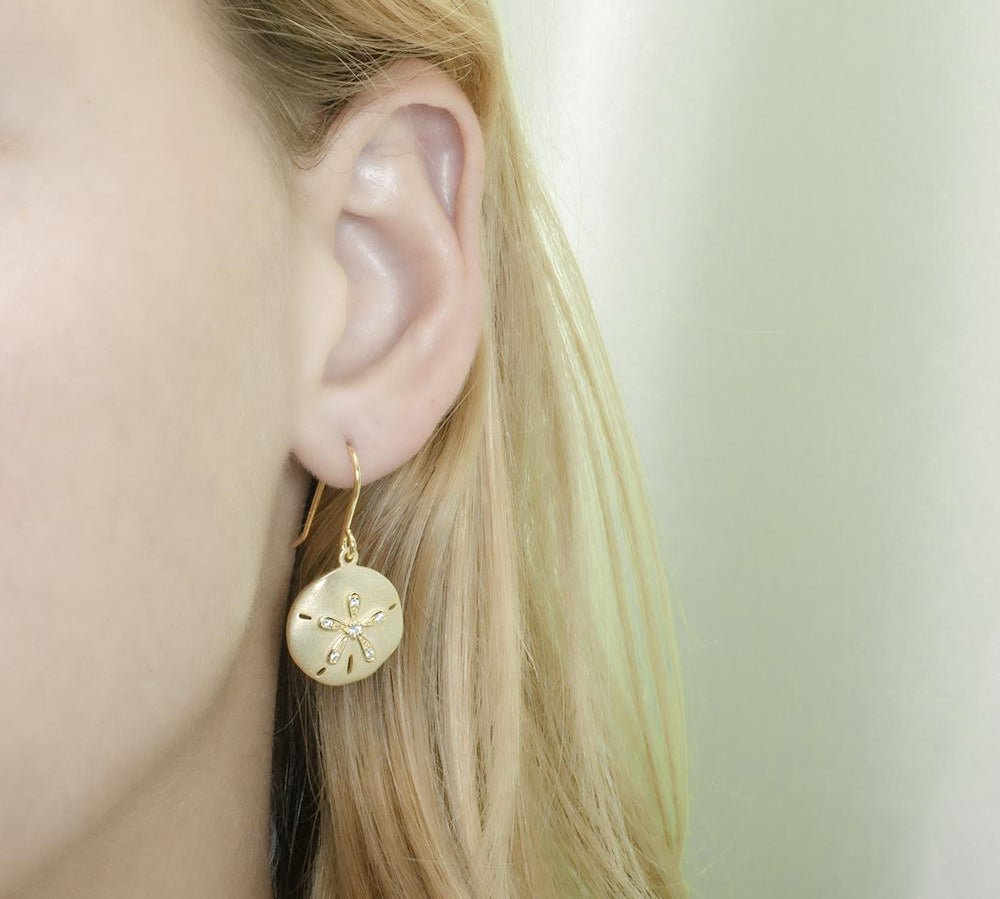 The picture shows a model wearing a yellow gold sand dollar hook earring with topaz.