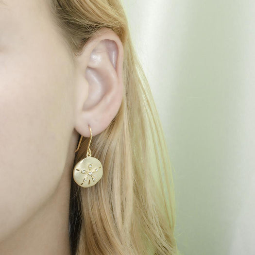 The picture shows a model wearing a yellow gold sand dollar hook earring with topaz.