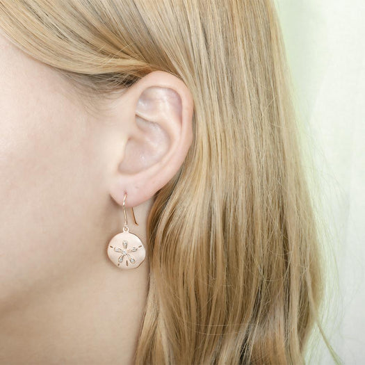 The picture shows a model wearing a rose gold sand dollar hook earring with topaz.