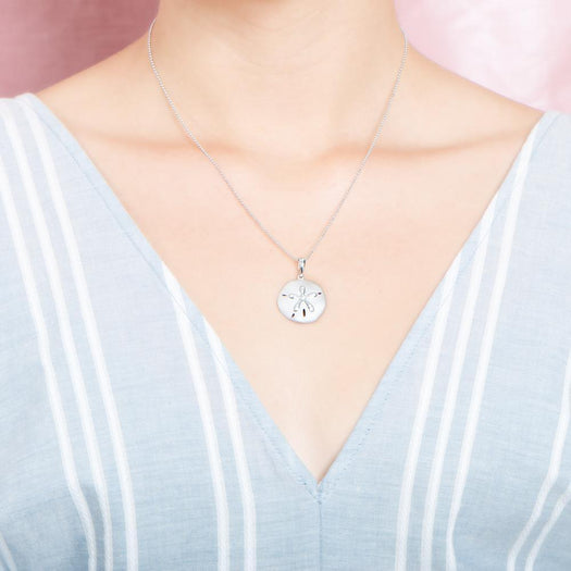 The picture shows a model wearing a white gold sand dollar pendant with topaz.