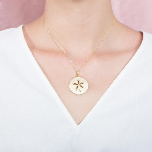 The picture shows a model wearing a 925 sterling silver, yellow gold plated, sand dollar cut out pendant with topaz.