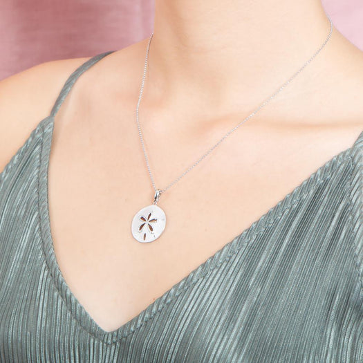 The picture shows a model wearing a 925 sterling silver, white gold plated, sand dollar cut out pendant with topaz.