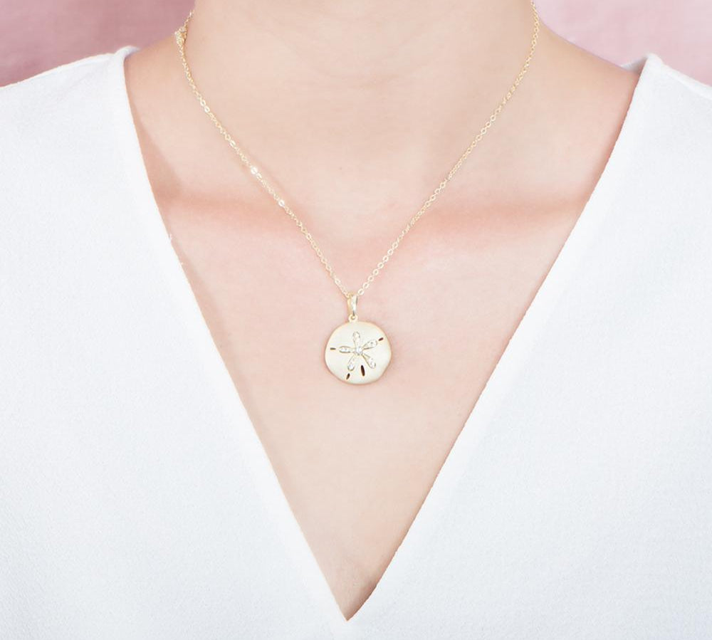 The picture shows a model wearing a yellow gold sand dollar pendant with topaz.