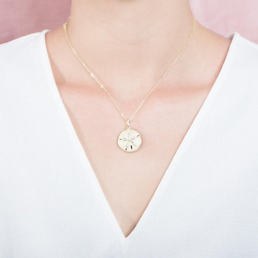 The picture shows a model wearing a yellow gold sand dollar pendant with topaz.