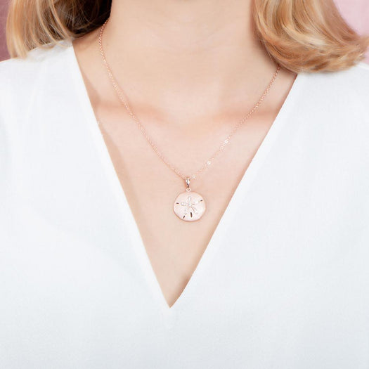 The picture shows a model wearing a rose gold sand dollar pendant with topaz.