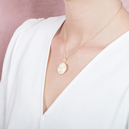 The picture shows a model wearing a yellow gold sand dollar pendant with topaz.