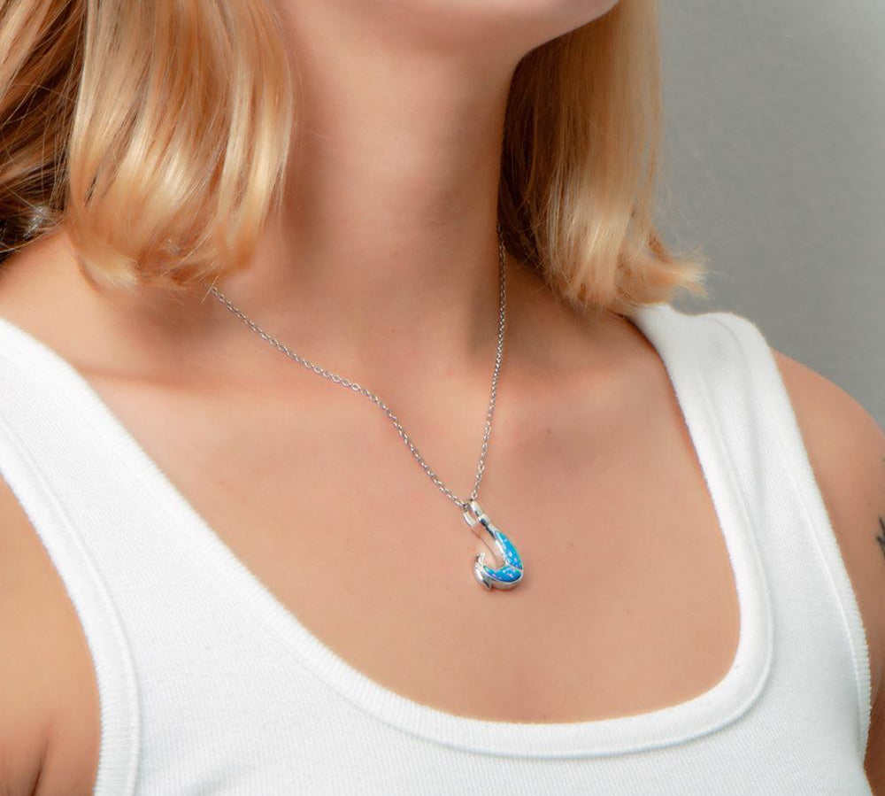 In this photo there is a model turned to the right with blonde hair and a white shirt, wearing a sterling silver fish hook pendant with blue opalite gemstones.