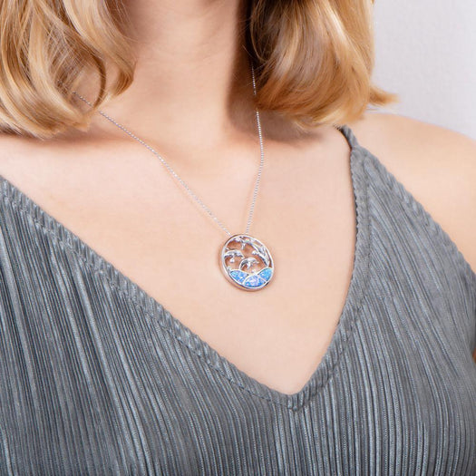 The picture shows a model wearing a 925 sterling silver opalite three jumping dolphins pendant with topaz.